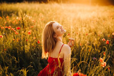 Kırmızı elbiseli güzel sarışın gün batımında çikolata parçacıklı kurabiye yiyor, gelincik tarlasında piknik yapıyor.