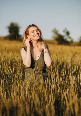 Şık takım elbiseli rüya gibi sarışın buğday tarlasında gözleri kapalı poz veriyor.