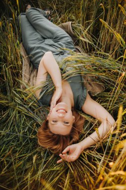 Yeşil takım elbiseli lüks sarışın gün batımında bir tarlada buğday başakları arasında yatıyor.