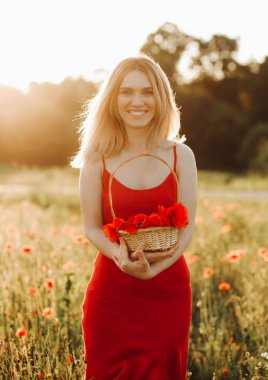 Haşhaş tarlasında poz veren kırmızı elbiseli güzel sarışın kadın elinde haşhaş dolu bir sepet tutuyor..