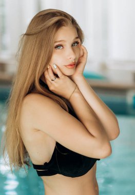 Siyah mayo giymiş iştah açıcı bir vücudu olan güzel bir sarışın havuz kenarında poz veriyor..