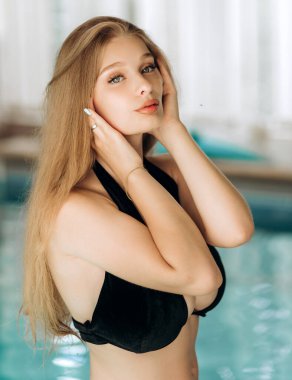 Siyah mayo giymiş iştah açıcı bir vücudu olan güzel bir sarışın havuz kenarında poz veriyor..