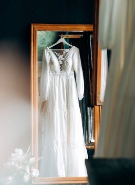 Sabahın yumuşak ışığında pencereye asılı modern gelinlik. Şık, gösterişli, dantel çiçekli bir gelinlik..