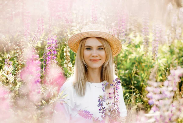 Hasır şapkalı mutlu sarışın Lupin tarlasında yürüyor..