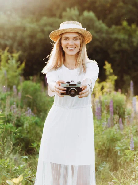 Hasır şapkalı bir kız çiçek tarlasında dikilip kamerasını gösteriyor.