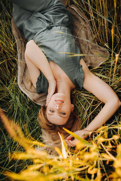 Luxury blonde in a green suit lies between ears of wheat in a field during sunset