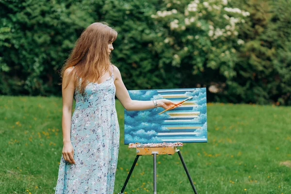 Harika bir kız parka resimli bir palet kullanarak resim çizer. Easel ve tuval..