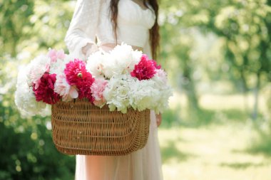 Elinde sepet dolusu taze şakayık tutan bir kadın. Bir buket pembe ve beyaz çiçek. Yaz duvar kağıdı.