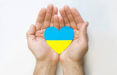 Ukrayna 'ya olan sevgi kavramı. Ukrayna bayrağının renginde bir kalp erkeklerin ellerinde beyaz bir arkaplanda.