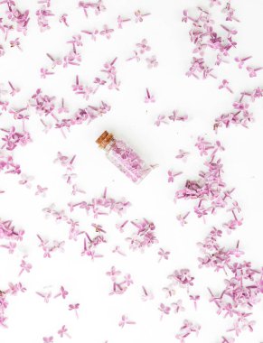 Kozmetik şişesi beyaz arka planda leylak çiçekleri ile kapanıyor.