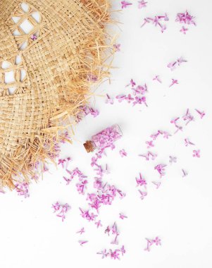 Beyaz arka planda saman bir şapkanın yanında duran leylak çiçekli şeffaf şişe.