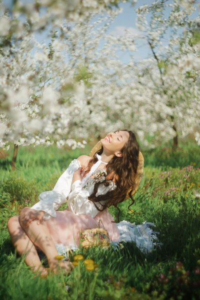 Picnic. In the soft light of spring sun there is an awesome woman hidden in the shadows of beautiful trees with white flowers