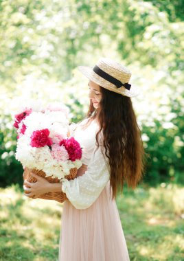 Hasır şapkalı mutlu bir kız elinde hasır bir sepet ile Avrupa 'nın sokaklarında poz veren beyaz ve pembe şakayık çiçekleri tutuyor. Yaşam biçimi