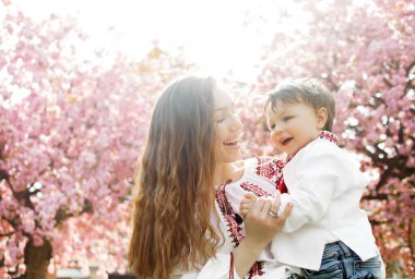 Annesinin ellerinde küçük bir çocuk. Çiçekli bahar bahçesinde çocukla oynayan bir kadın..