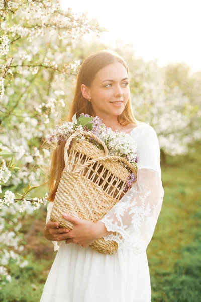 Young attractive woman of natural beauty with basket of flowers in summer garden enjoying the blooming spring nature