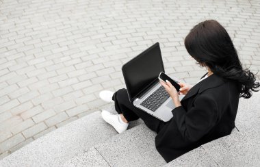 Laptopta çalışan meşgul bir kadın, parkta merdivenlerde oturan serbest çalışan biri..