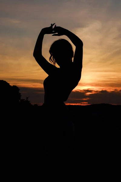 Close up silhouette of dancing woman at sunset. Image against the sun and orange sky.