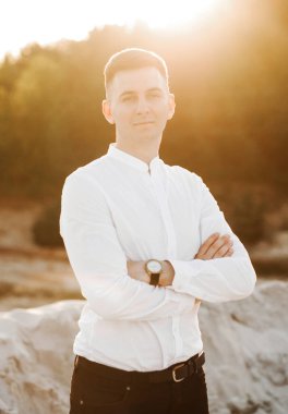 Cute guy in white shirt and black pants at sunset