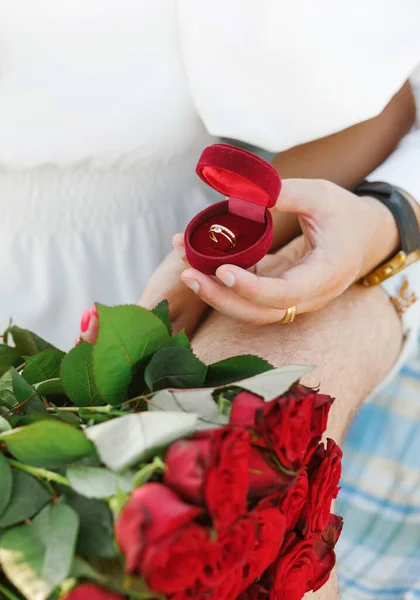 Marriage proposal. Red box with a ring and roses on the background of the couple.