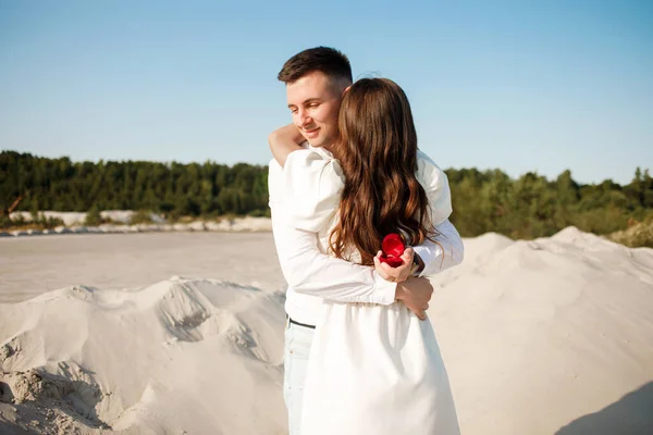 Photo of man making proposal to his amazed woman with ring in gift box while walking on sunny beach
