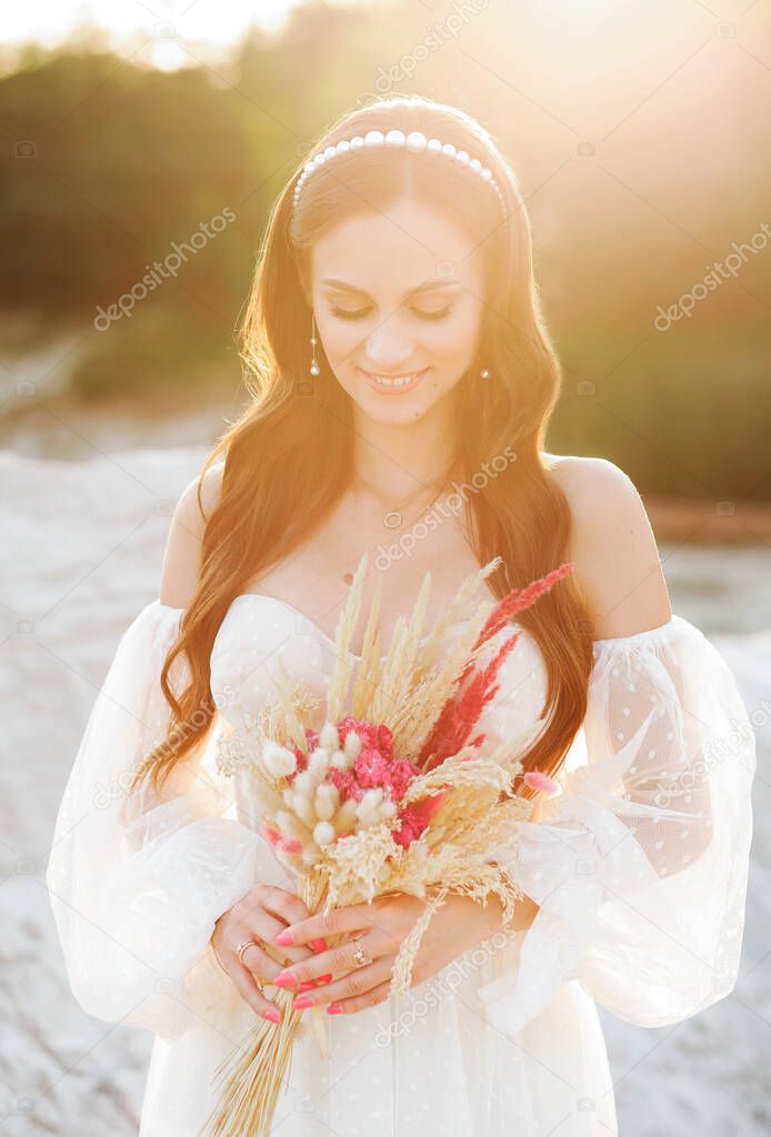 Beautiful girl in wedding dress posing in sand canyon with a bouquet in her hands