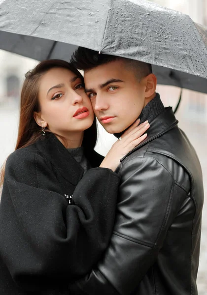 Sweet couple boy and girl hugging under an umbrella in the rain. The concept of love, romance and passion.
