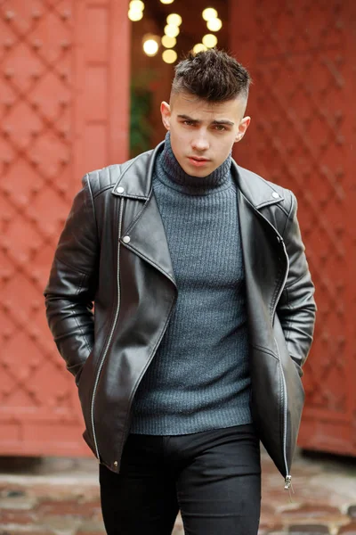 Stylish man with a fashionable hairstyle in a leather jacket posing on the street in motion.