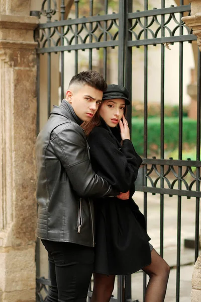 Stylish couple posing near a wrought iron gate in the yard.