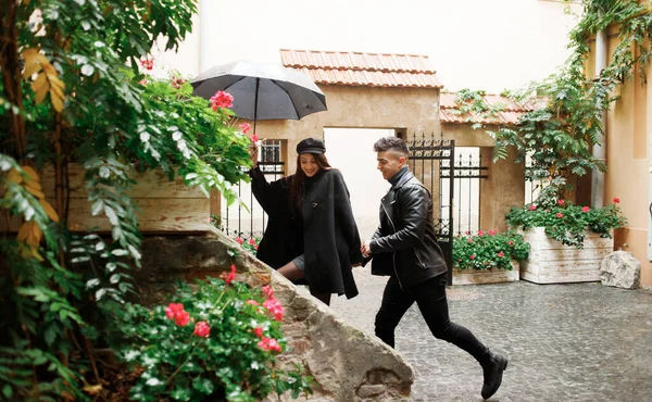 The sweet couple running in the yard under an umbrella in rainy weather.