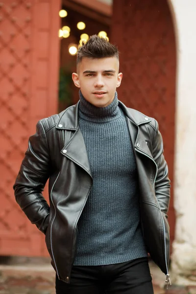 Stylish man with a fashionable hairstyle in a leather jacket posing on the street in motion.
