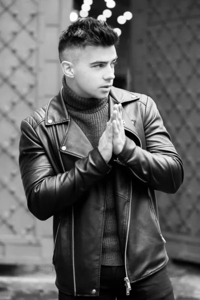 Fashionable man in a black leather jacket posing on the background of the gate.