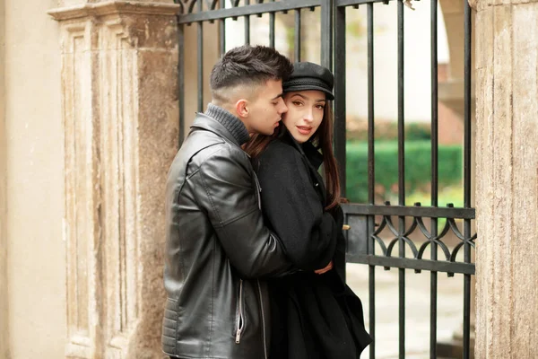 Stylish couple posing near a wrought iron gate in the yard.