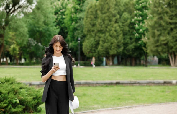 Business woman talking on a mobile phone outdoors, professional woman in a suit walking along an park, checking her smartphone