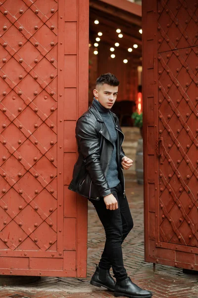 Fashionable man in a black leather jacket posing on the background of the gate.