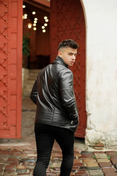 Stylish man with a fashionable hairstyle in a leather jacket posing on the street in motion.
