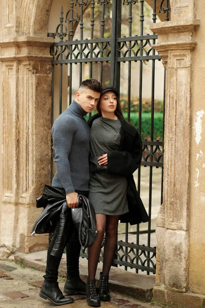 Stylish couple posing near a wrought iron gate in the yard.