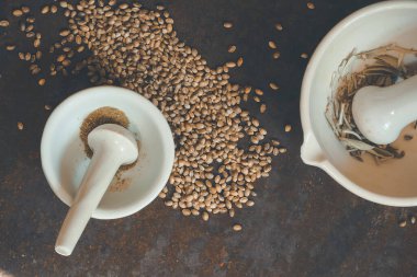 Haşlanmış kenevir tohumu ve kurutulmuş adaçayı otları eski beyaz seramik havan ve tokmak ile kaba bir masa yüzeyinde, üst görünüm