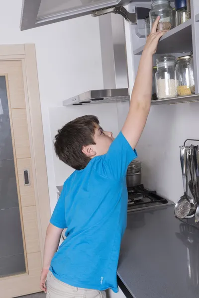 Kleiner Junge nimmt Süßigkeiten aus einem hohen Küchenschrank — Stockfoto