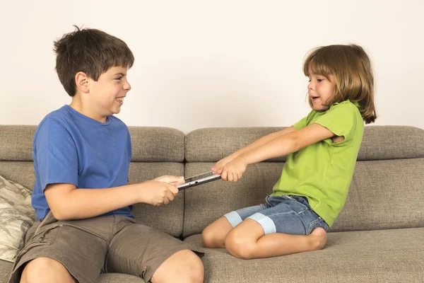 Barn argumenterar för att spela med en digital tablett på en soffa. — Stockfoto