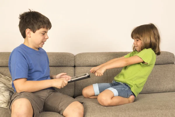 Crianças discutindo para brincar com um tablet digital em um sofá . — Fotografia de Stock