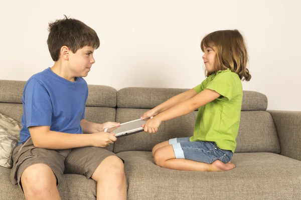 Enfants argumentant pour jouer avec une tablette numérique sur un canapé . — Photo