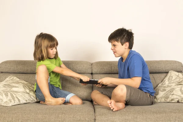 Crianças discutindo para brincar com um tablet digital em um sofá . Imagem De Stock