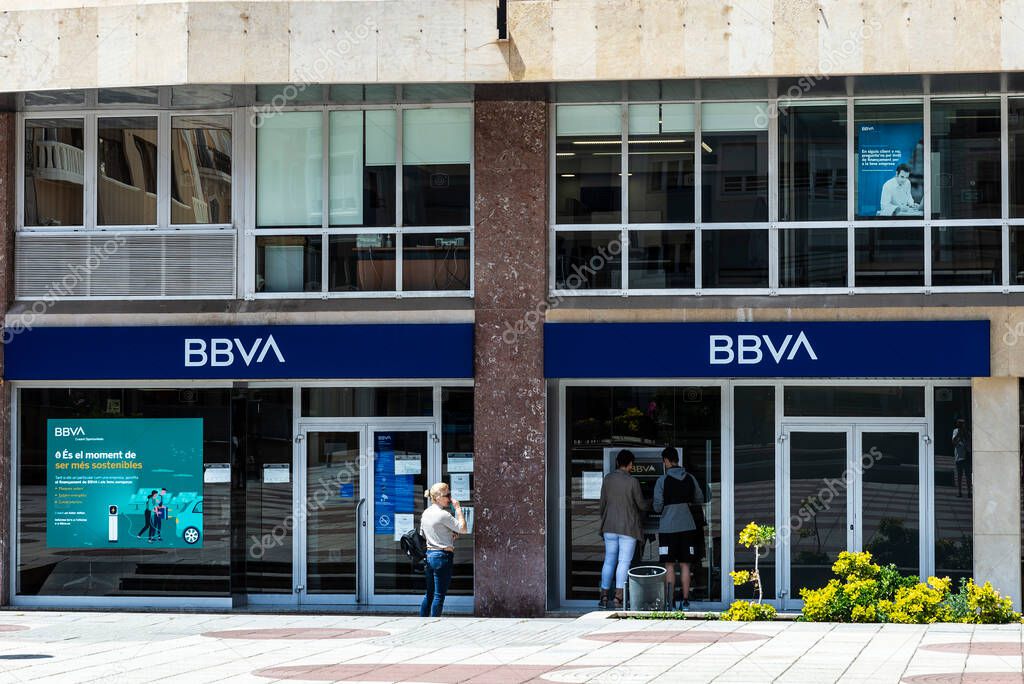 Tortosa, Spain - May 13, 2022: Facade and logo of the Banco Bilbao Vizcaya Argentaria or BBVA with people at the ATM in Tortosa, Catalonia, Spain