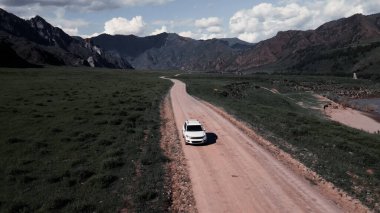 Dağlarda dar bir yoldan beyaz bir araba geçiyor. İnsansız hava aracı görüntüleri