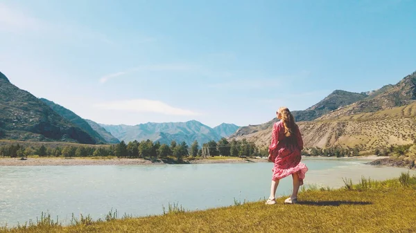 Señora en vestido rojo largo con vistas a la orilla de dos ríos con montañas en el fondo. Imágenes de drones —  Fotos de Stock
