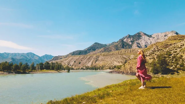 女性の長い赤いドレスの背景に山と2つの川の端を見下ろす。ドローン映像 — ストック写真