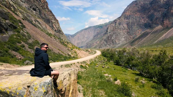 Um homem senta-se à beira de um penhasco usando um anoraque preto. Katu-Yaryk desfiladeiro Chulyshman Valley. Altai... — Fotografia de Stock