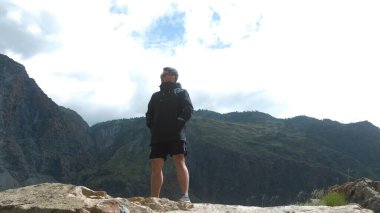 Uçurumun kenarında siyah bir anorak giyen bir adam. Katu-Yaryk Kanyonu Chulyshman Vadisi. Altai.