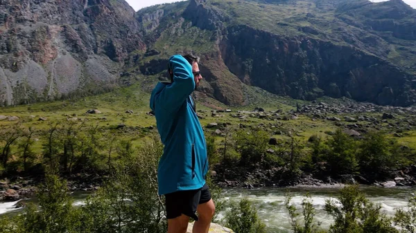 青いアナークをした崖の端に眼鏡をかけた男が腰を下ろしている。カトゥヤリク峡谷チュリシュマン渓谷。アルタイ — ストック写真