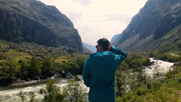青いアナークをした崖の端に眼鏡をかけた男が腰を下ろしている。カトゥヤリク峡谷チュリシュマン渓谷。アルタイ — ストック写真